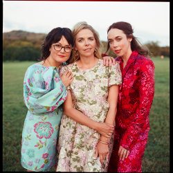 Three women posing for portrait in green field.